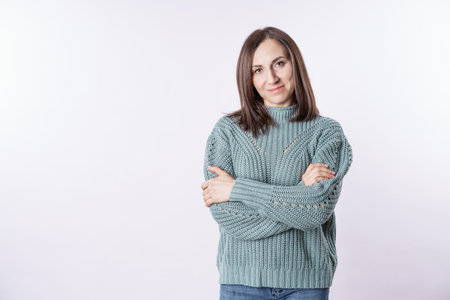 A woman is wearing a green sweater and is standing with her arms crossed. She has a serious...