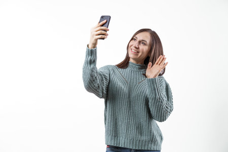 A woman is taking a selfie with her cell phone. She is wearing a green sweater and smilingの写真素材