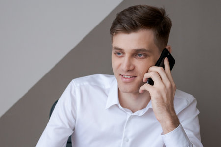 man is talking on his cell phone while sitting at desk He is smiling and he is enjoying the...