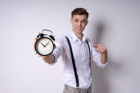 A man is holding a clock that is showing the time. He is pointing to the clock and smiling,...