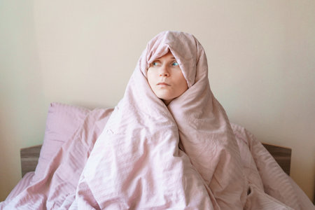 A woman is wrapped in a pink blanket and is looking at the camera. Concept of warmth and comfort, as the woman is snugly wrapped in the blanketの写真素材