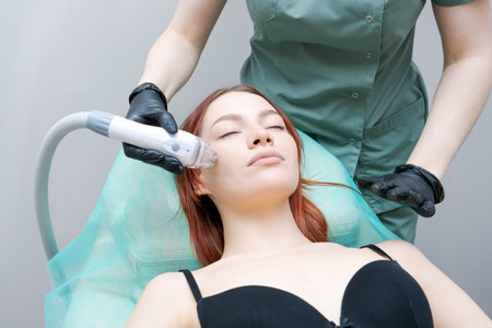 A woman is getting a facial treatment with a device that looks like a hair dryer. The woman is wearing a black bra and a green clothの写真素材
