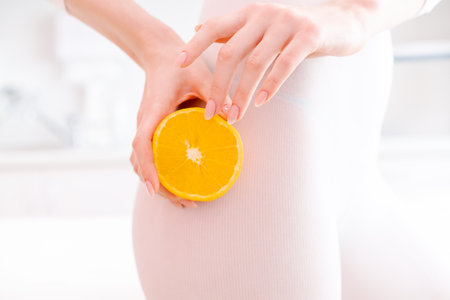 A woman holding an orange in her hand. The orange is cut in half and is placed on her thighの写真素材