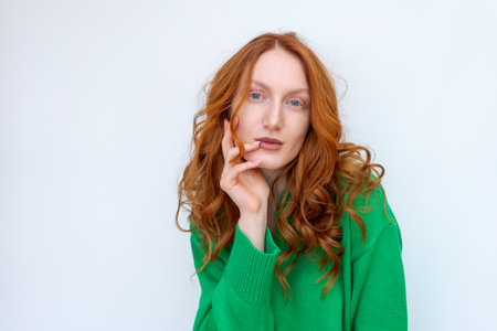 A woman with red hair is wearing a green sweater and is looking at the camera. She has a serious expression on her faceの写真素材