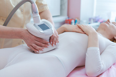 A woman is getting a body contouring treatment. The woman is laying on a table and a technician is holding a device on her stomachの写真素材