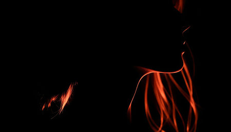 A woman's silhouette is shown in a black background with orange hair. Concept of mystery and intrigue, as the woman's face is obscured by the darkness and the glowing hairの素材