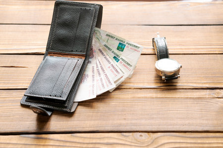 A wallet with a watch and a stack of bills. The wallet is black and the watch is silverの写真素材