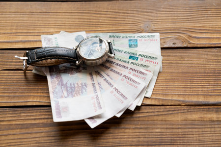 A watch is on top of a pile of money. The watch is black and silver. The money is in Russianの写真素材