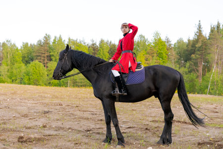 Man in a red coat is riding a black horse in a field. The man is looking to his rightの素材