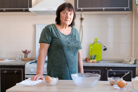 Woman is standing in a kitchen with a bowl of eggs on the counter. She is wearing a green shirt and she is in a bad moodの写真素材