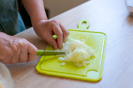Person is cutting onions on a green cutting board. The onions are being chopped into small piecesの写真素材