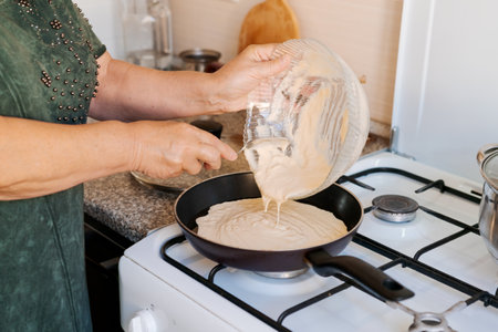 Woman is making a dessert in a kitchen. She is pouring a white liquid into a pan on a stoveの写真素材