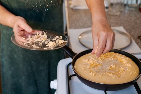Woman is making a cheese pizza in a pan. She is sprinkling cheese on top of the pizza
