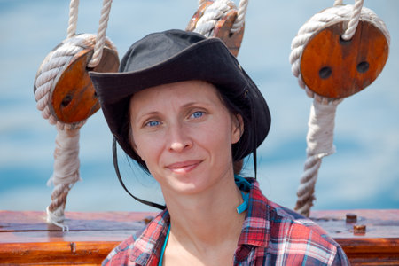 Woman wearing a black hat and a red and white plaid shirt is smiling. She is standing on a boat with ropes hanging from the ceilingの写真素材