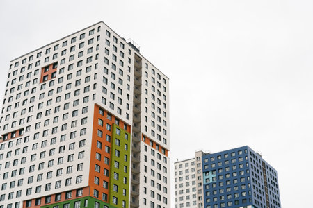 Two tall buildings with windows and a blue one. The buildings are in front of a cloudy skyの写真素材