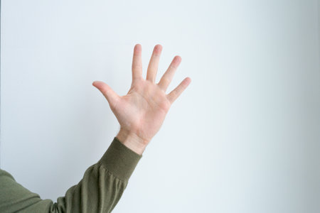 Man is wearing a green sweater and is holding up his hand with the fingers spread out. Concept of...