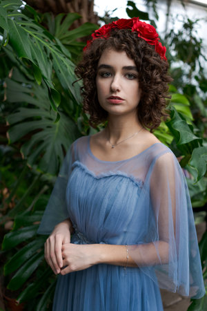 Woman wearing a blue dress and a red flower headband. She is standing in front of a green plantの写真素材