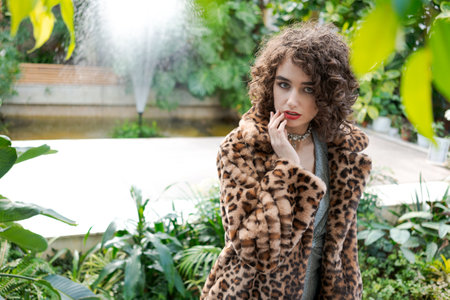 Woman wearing a leopard print coat poses in front of a fountain. She is wearing a necklace and has red lipstick onの写真素材