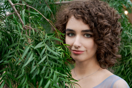 Woman with brown hair is standing in front of a tree. She is wearing a blue dress and a necklaceの写真素材