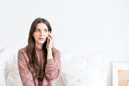 Woman is talking on her cell phone. She is wearing a pink sweater. The room is whiteの写真素材