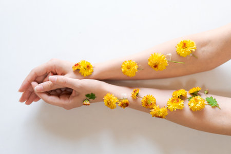 The hands decorated with yellow flowers lie on a light background, creating a bright and cheerful compositionの写真素材