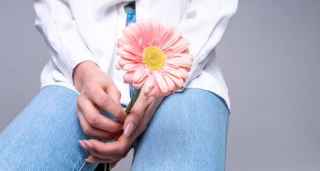 Woman holding pink gerbera standing in jeans and white blouse on light background. Ideal for fashion, cosmetics or floristry and health advertisingの写真素材