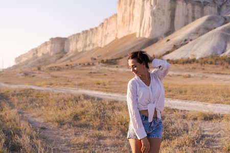 Woman is standing in a desert with a white shirt and blue shorts. She is smiling and looking at the cameraの写真素材