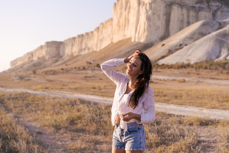Woman is standing in a field with her hair down. She is wearing a white shirt and denim shortsの写真素材