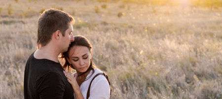 Man and a woman are hugging in a field. The man is wearing a black shirtの写真素材