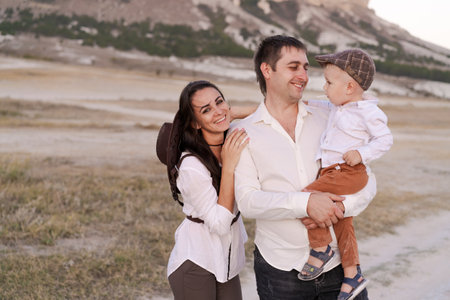 Man and a woman are holding a baby. The man is wearing a hat. The baby is wearing a white shirt