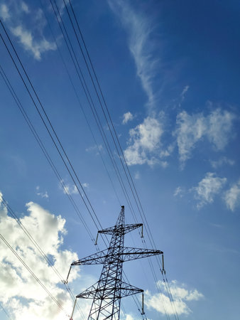 Tall power tower with wires above it. The sky is blue with some clouds