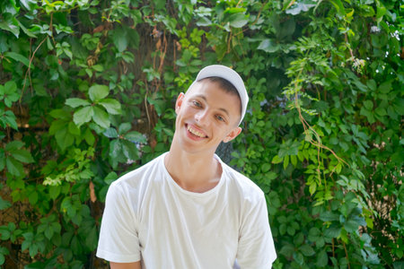 Man is smiling and wearing a white shirt. He is standing in front of a green wall
