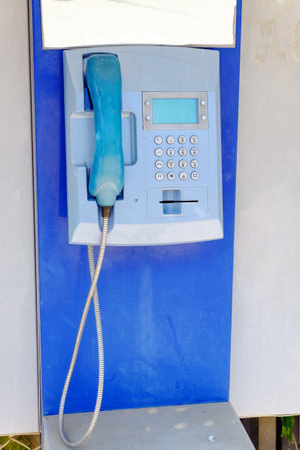 Blue phone with a cord hanging out of it is on a blue wall. The cord is attached to the phone, and...