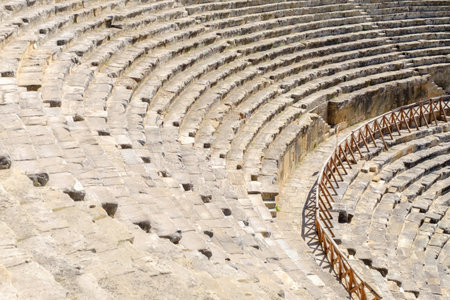 The image shows an ancient stone amphitheater with empty seating areas and a wooden barrier on one...