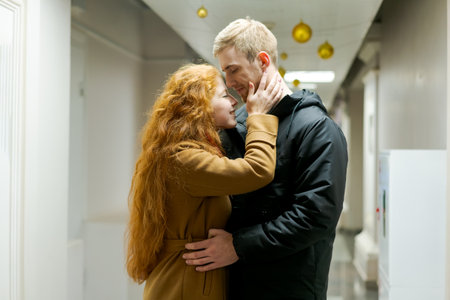 Man and a woman are hugging in a hallway. The man is wearing a black jacket. The woman has red hair