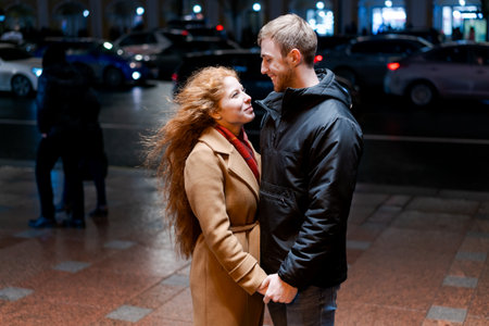 Man and a woman are standing on a sidewalk. The man is wearing a black jacket and the woman is wearing a brown coatの写真素材