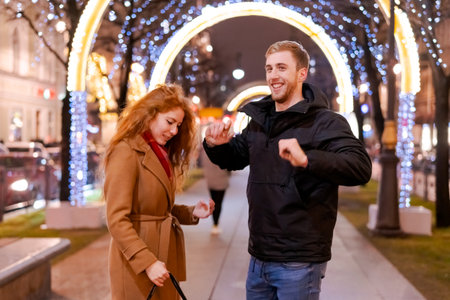 Man and a woman are standing on a sidewalk. The man is wearing a black jacket and the woman is...