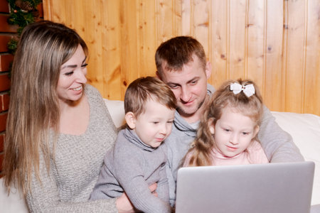 Family of four is sitting on a bed and looking at a laptop. A woman is holding a childの写真素材