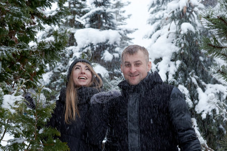 Man and a woman are standing in the snow, smiling at the camera. They are both wearing black jackets