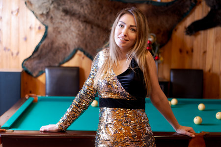 Woman in a gold and black dress stands in front of a pool table. There are three balls on the table