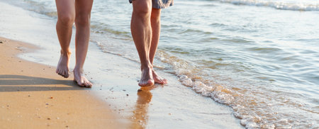 Two people walking on the beach. One is wearing shorts. The other is wearing a bikini. The water is calmの写真素材