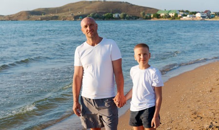 Man and a boy are walking on the beach. The man is holding the boy's hand