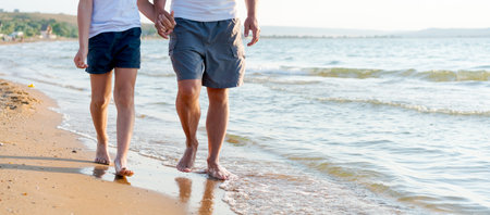 Two people walking on the beach. One is wearing shorts and the other is wearing a white shirtの写真素材