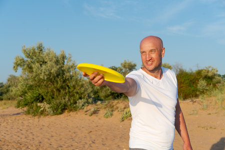Man is holding a yellow frisbee and is standing on a sandy beach. He is smiling and he is enjoying himselfの写真素材