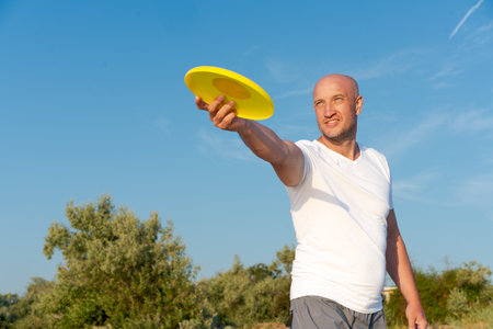 Man is holding a yellow frisbee in his hand. He is smiling and looking up at the skyの写真素材