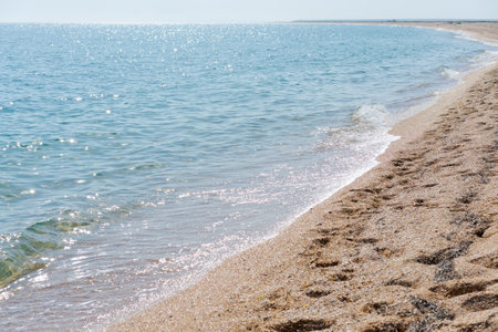 The ocean is calm and the water is clear. The beach is sandy and there are footprints in the sandの写真素材