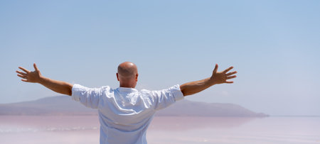 Man is standing on a beach and is reaching out with his hands. The sky is blue and clearの写真素材
