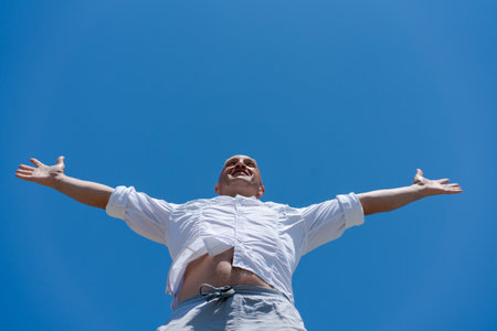 Man is standing in the air with his arms outstretched. He is wearing a white shirt and gray shortsの写真素材