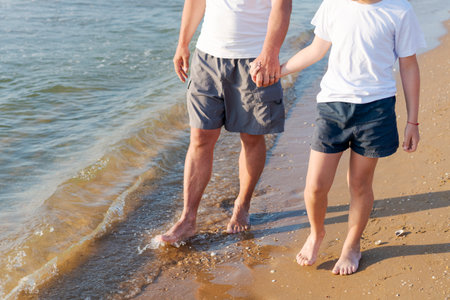 Man and a child are walking on the beach. The man is holding the child's handの写真素材