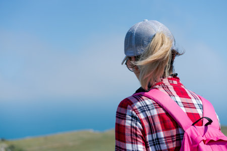 Woman with blonde hair and a pink backpack is looking out over the ocean. She is wearing a white hatの写真素材
